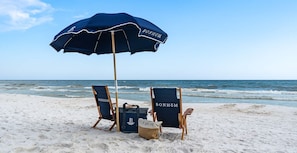 Une scène de plage avec deux chaises de plage en bois, un parasol bleu et un sac de plage.
