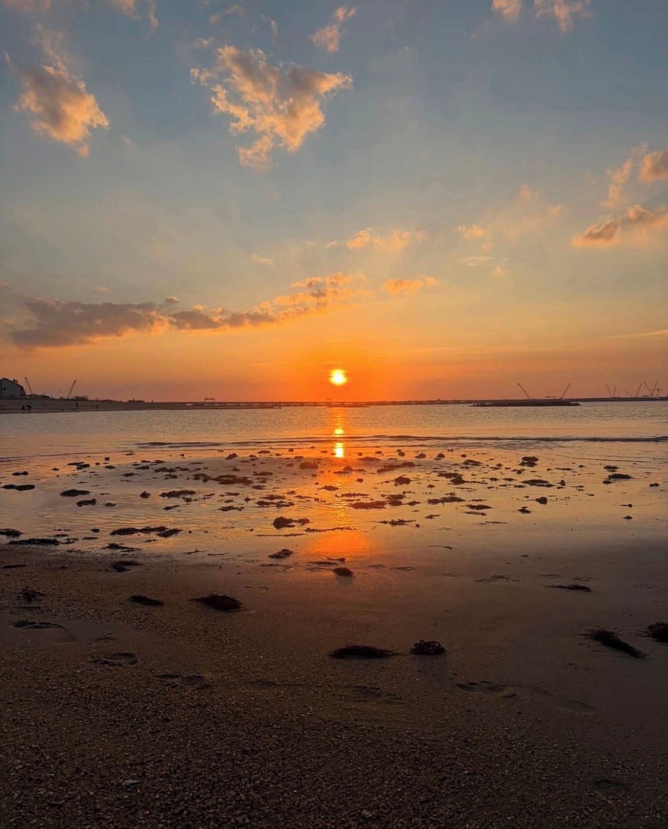 A beach at sunset with the sun low on the horizon, reflecting on the wet sand.