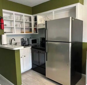 A kitchen with white cabinets, a stainless steel refrigerator, a microwave, and a coffee maker.