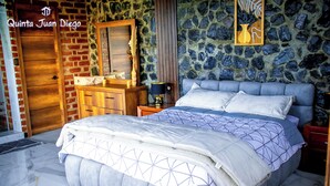 Une chambre avec un grand lit, une commode en bois, un mur en pierre et un miroir.