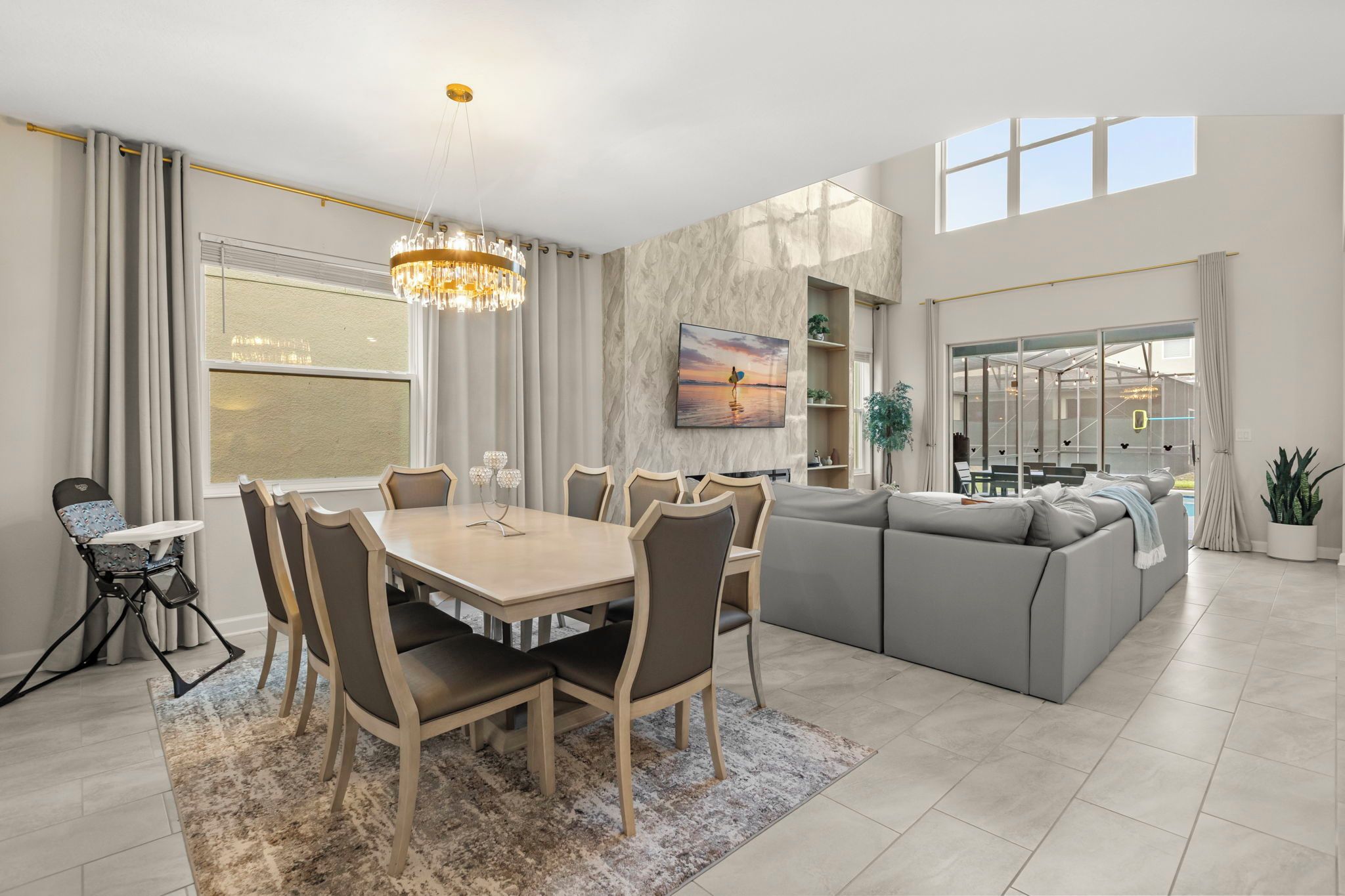 Een moderne woonkamer met een eethoek, een bank, een kroonluchter en een groot raam.