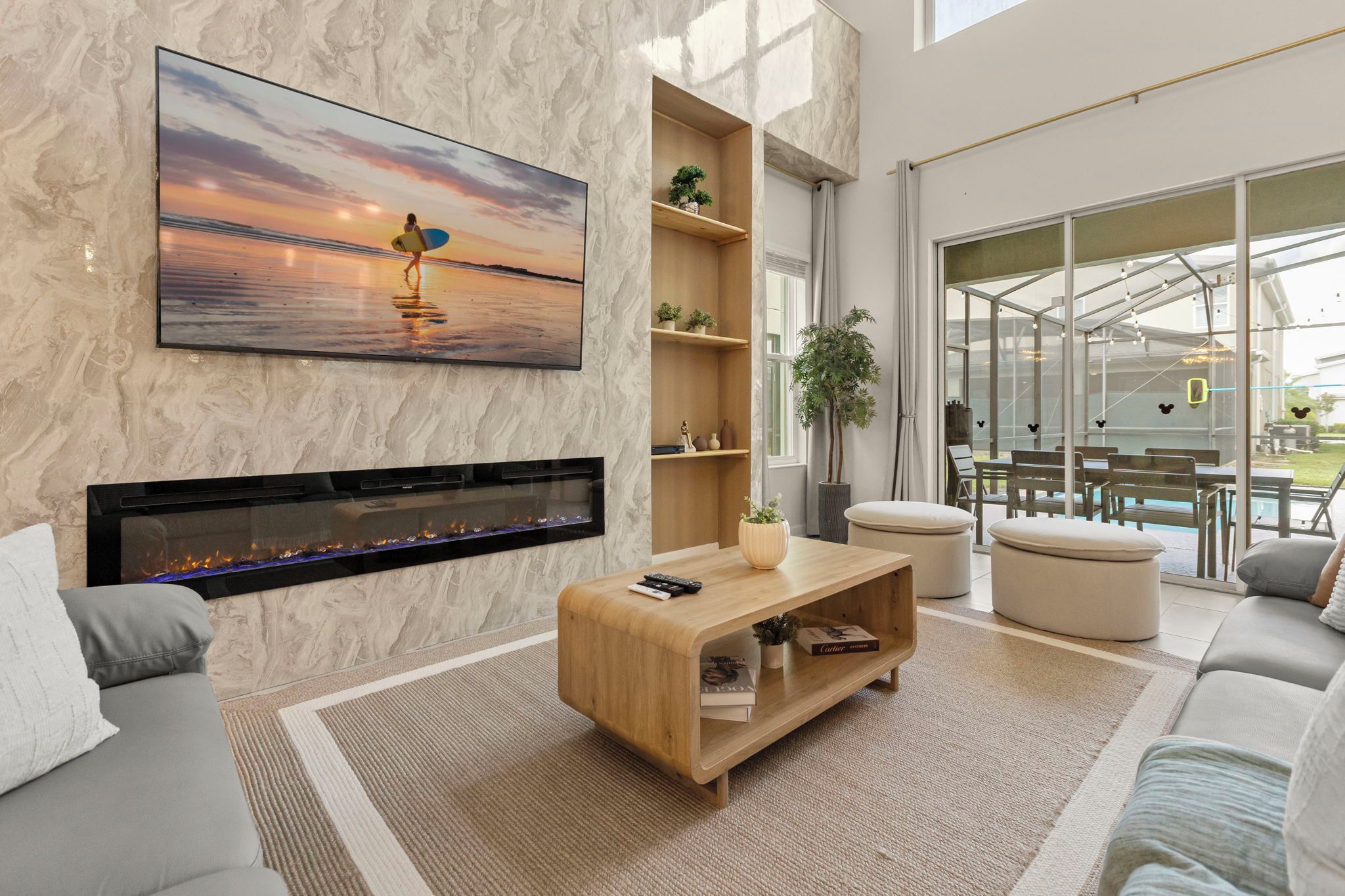 Uma sala de estar moderna com lareira, uma televisão grande fixada na parede e vista para o exterior através de amplas janelas.