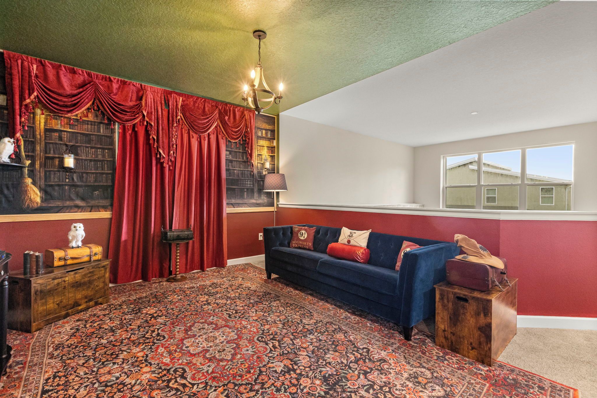 A room with a large bookshelf, a blue sofa, a patterned rug, and a window with a view of buildings.