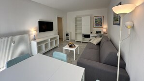 A modern living room with a flat-screen TV, a sofa, a dining table, and a white radiator. - VEILLITH (Cannes)