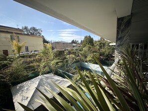 A balcony with a view of a courtyard, a pool, and surrounding buildings.