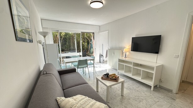 A modern living room with a sofa, a coffee table, a TV, and a dining area with chairs and a table. - VEILLITH (Cannes)