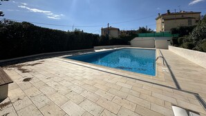 A swimming pool with a tiled deck, surrounded by a hedge and buildings in the background. - VEILLITH (Cannes)