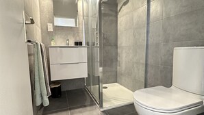 A modern bathroom with a glass shower enclosure, a white toilet, and a vanity with a mirror. - VEILLITH (Cannes)