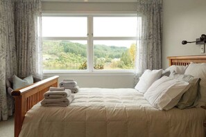 A bedroom with a large window, a bed with white bedding, and a view of a forested area.