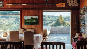 Una habitación acogedora con detalles de madera, un comedor y un gran ventanal con vistas panorámicas a un lago y colinas.