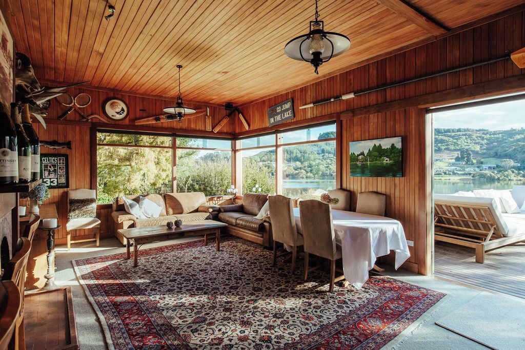 Interior acogedor de una cabaña con paredes de madera, un ventanal grande con vistas a un lago, una zona de comedor y un espacio de estar con vistas.