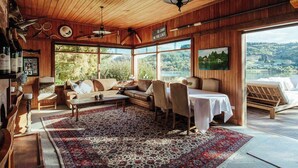 Interior acogedor de una cabaña con paredes de madera, un ventanal grande con vistas a un lago, una zona de comedor y un espacio de estar con vistas.