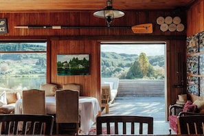 Una habitación acogedora con detalles de madera, un comedor y un gran ventanal con vistas panorámicas a un lago y colinas.