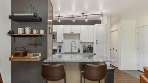 A modern kitchen with white cabinets, a granite countertop, and two bar stools.