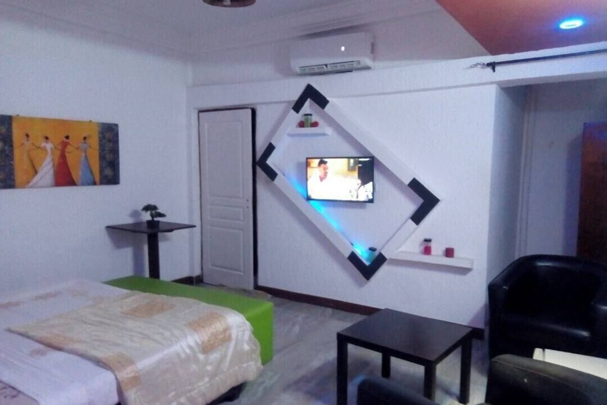 A hotel room with a bed, a desk, a chair, a TV mounted on the wall, and a painting on the wall.
