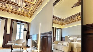 A spacious living room with a large mirror, wooden flooring, and a high ceiling with intricate designs. - YOUROPO - Collection (Porto)