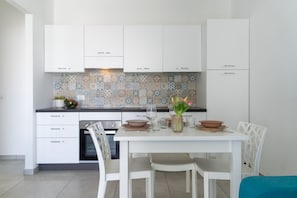 Une cuisine moderne avec des meubles blancs, un dosseret carrelé et une table à manger pour quatre personnes.