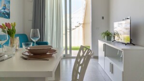 A dining area with a table set for two, a TV on a cabinet, and a view through a glass door.
