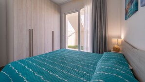 A bedroom with a bed, a nightstand, a lamp, a window with curtains, and a door.