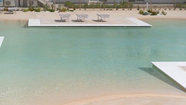 A swimming pool with three lounge chairs and a concrete deck.