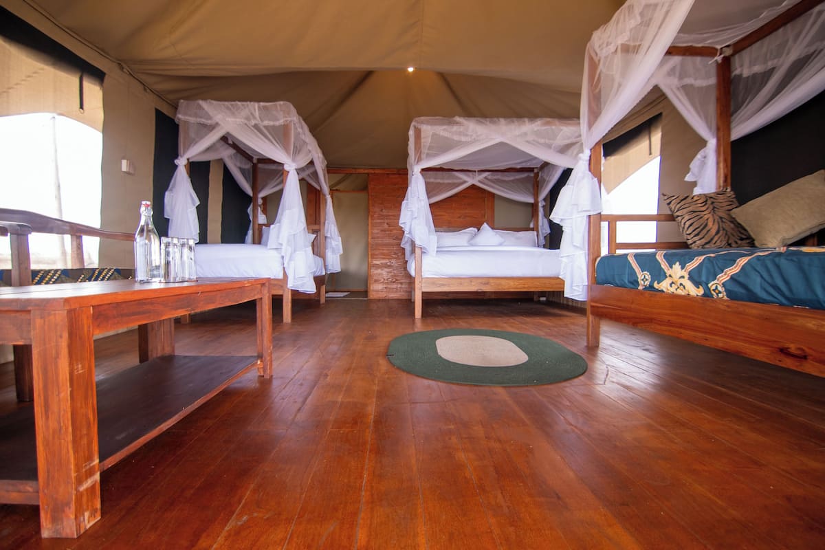 A room with two beds, each with a canopy, a wooden table, and a bench.