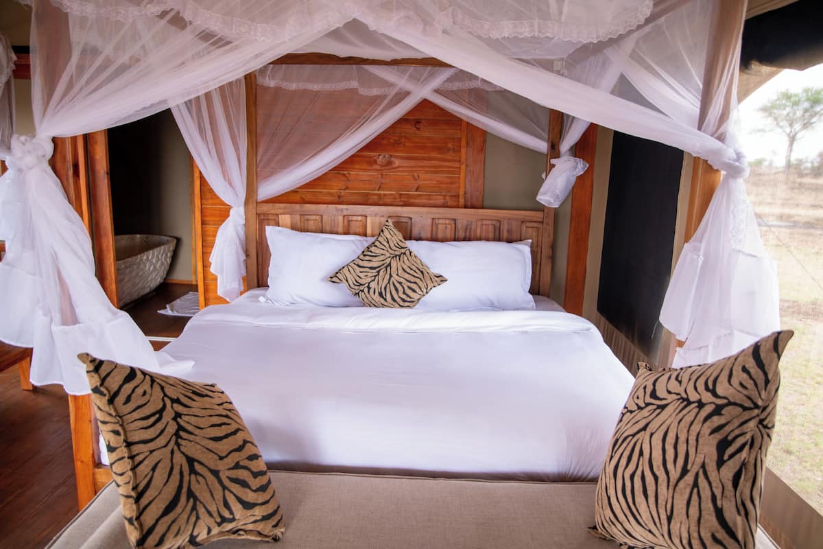 A bed with a canopy, white bedding, and two tiger-patterned pillows.