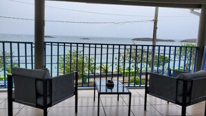 Un balcon avec deux chaises et une petite table, donnant sur une étendue d’eau et sur de la verdure.