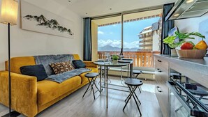 A modern living room with a yellow sofa, a dining table, and a balcony with a mountain view.