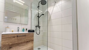 A modern bathroom with a glass-enclosed shower, a wooden vanity with a mirror, and a white tiled wall.