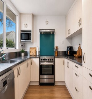A modern kitchen with stainless steel appliances, white cabinetry, and a teal backsplash.