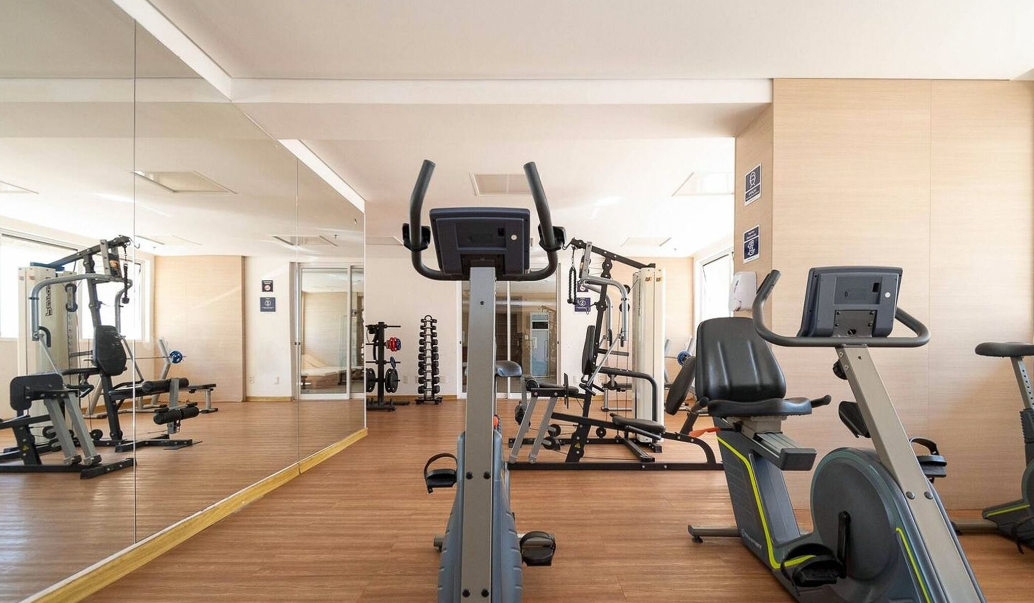 Ein Fitnessstudio mit Cardiogeräten, Gewichten und einer Spiegelwand.