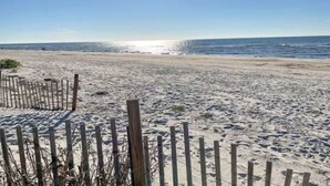 Una playa arenosa con una valla de madera en primer plano y el océano al fondo.