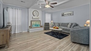 Un salón con suelo de madera, ventilador de techo, sofá, mesa de centro y televisor sobre un mueble de madera.