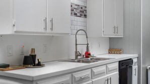 Una cocina moderna con armarios blancos, un lavamanos de acero inoxidable y un lavavajillas.