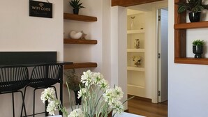 Una habitación moderna con comedor, estantes de madera con plantas y una puerta que conduce a otra habitación.
