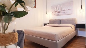 Un dormitorio con cama, un florero con flores, un cuadro en la pared y una lámpara colgante.