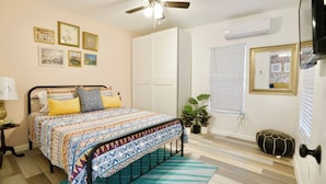 A bedroom with a bed, ceiling fan, wall-mounted air conditioner, and framed pictures. - Casa Blanca near Downtown (San Antonio)