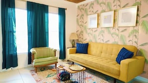A living room with a yellow sofa, green armchair, and a patterned rug. There are three framed pictures on the wall and a lamp on a side table. - Casa Blanca near Downtown (San Antonio)