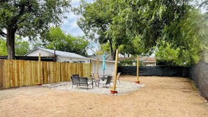 A backyard with a wooden fence, a patio area with chairs and a table, and a blue umbrella. - Casa Blanca near Downtown (San Antonio)