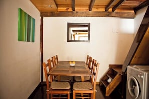 Uma área de refeições com mesa e cadeiras de madeira, uma janela pequena e uma máquina de lavar.