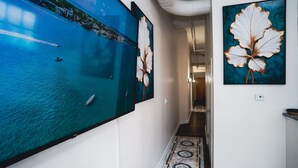 Un pasillo con un mural grande de una escena costera, un tapiz estampado y dos obras de arte enmarcadas.