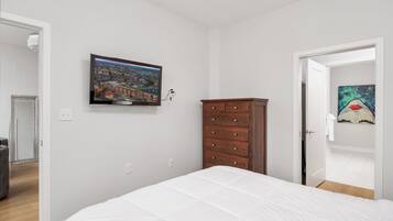A bedroom with a bed, a dresser, a television on the wall, and a door leading to another room.