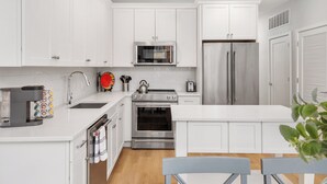 Une cuisine moderne avec des meubles blancs, des appareils en acier inoxydable et un îlot central.