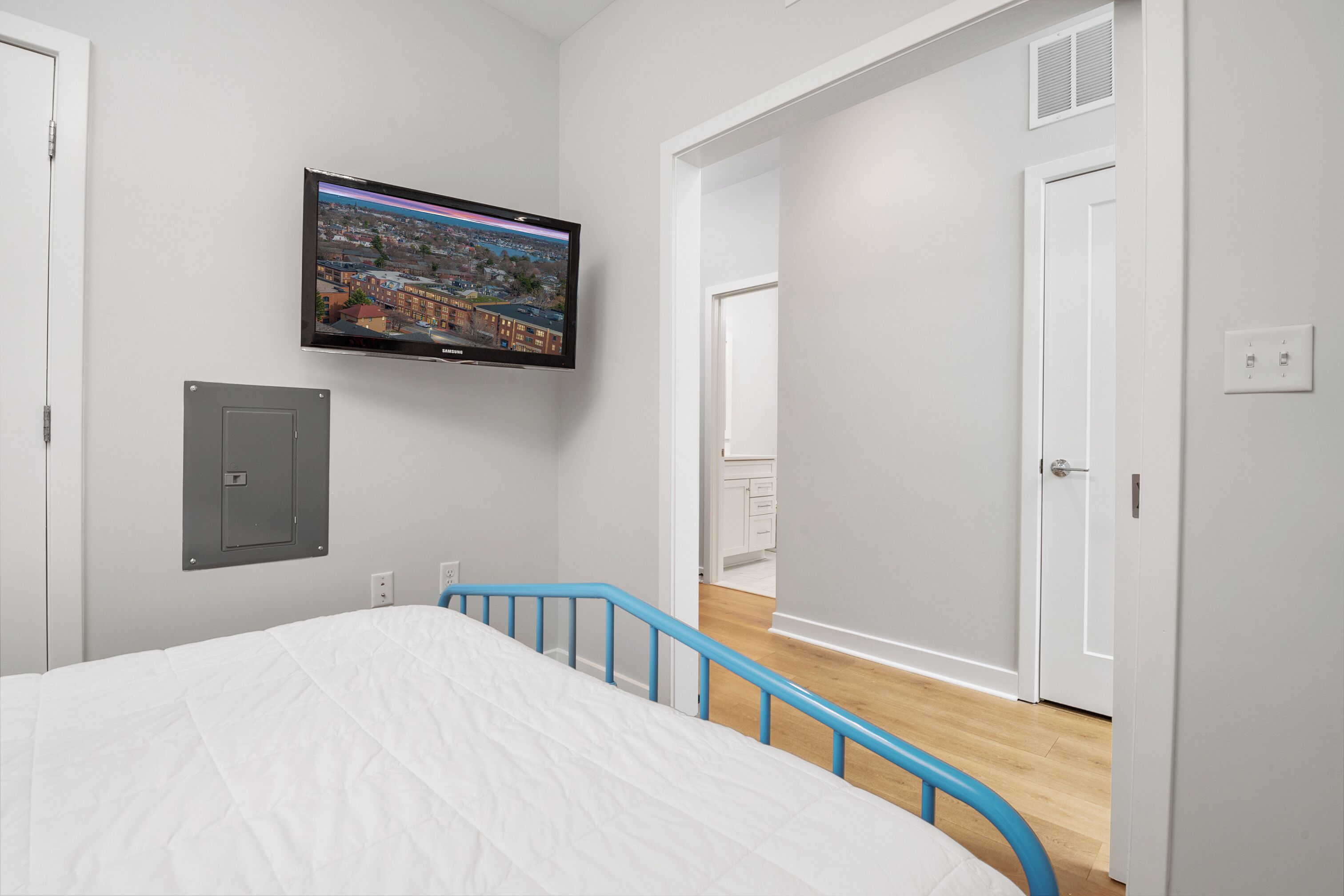 Ein Schlafzimmer mit einem Bett, einem Wand-Fernseher, einer Tür und einem Flur, der in einen anderen Raum führt.
