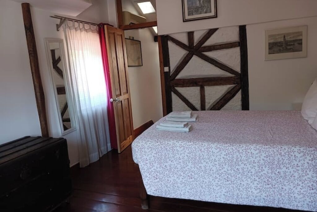 A bedroom with a bed, a wooden wardrobe, a door with a curtain, and a wall with a wooden beam design.