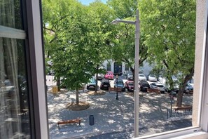 Vista desde una ventana que muestra un estacionamiento con árboles, coches aparcados y un farol.
