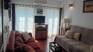 Una sala de estar con un sofá, una mesa de centro, un televisor sobre un mueble bajo y una lámpara.