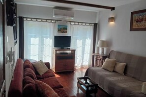 Una sala de estar con un sofá, una mesa de centro, un televisor sobre un mueble bajo y una lámpara.