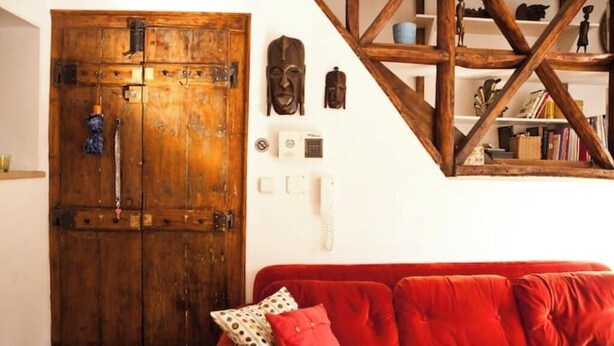 Una habitación con un armario de madera, un sofá rojo y una estantería con objetos decorativos.