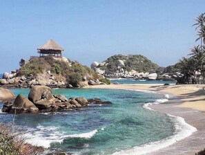 A beach with clear turquoise waters, large rocks, and a thatched-roof structure on a hill. - Private luxury jacuzzi in Pozos Colorados (Magdalena)